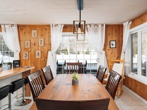 Une salle à manger aux murs lambrés, avec une grande table, des chaises et un luminaire suspendu.