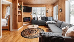 Acogedor interior de una cabaña de madera con sofá, televisión y chimenea.