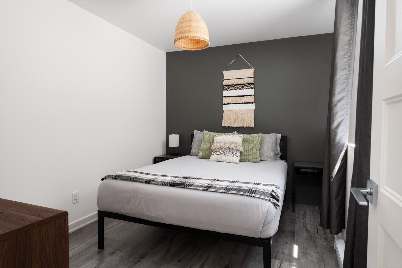 Een slaapkamer met een bed, nachtkastjes, een hanglamp en een wandtapijt.