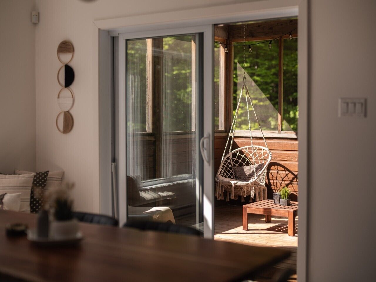 A room with a sliding glass door leading to an outdoor seating area with a hanging chair and a wooden bench.