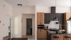A modern kitchen with wooden cabinets, a black countertop, and two bar stools. - Chalet Röcka with hot tub and lake access! (Chertsey)