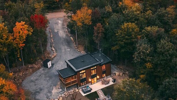 A modern house surrounded by dense forest with a driveway leading to the entrance. - Chalet Röcka with hot tub and lake access! (Chertsey)