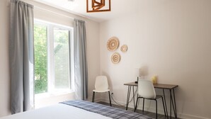 A bedroom with a bed, a desk, two chairs, a window with curtains, and wall decor. - Chalet Röcka with hot tub and lake access! (Chertsey)