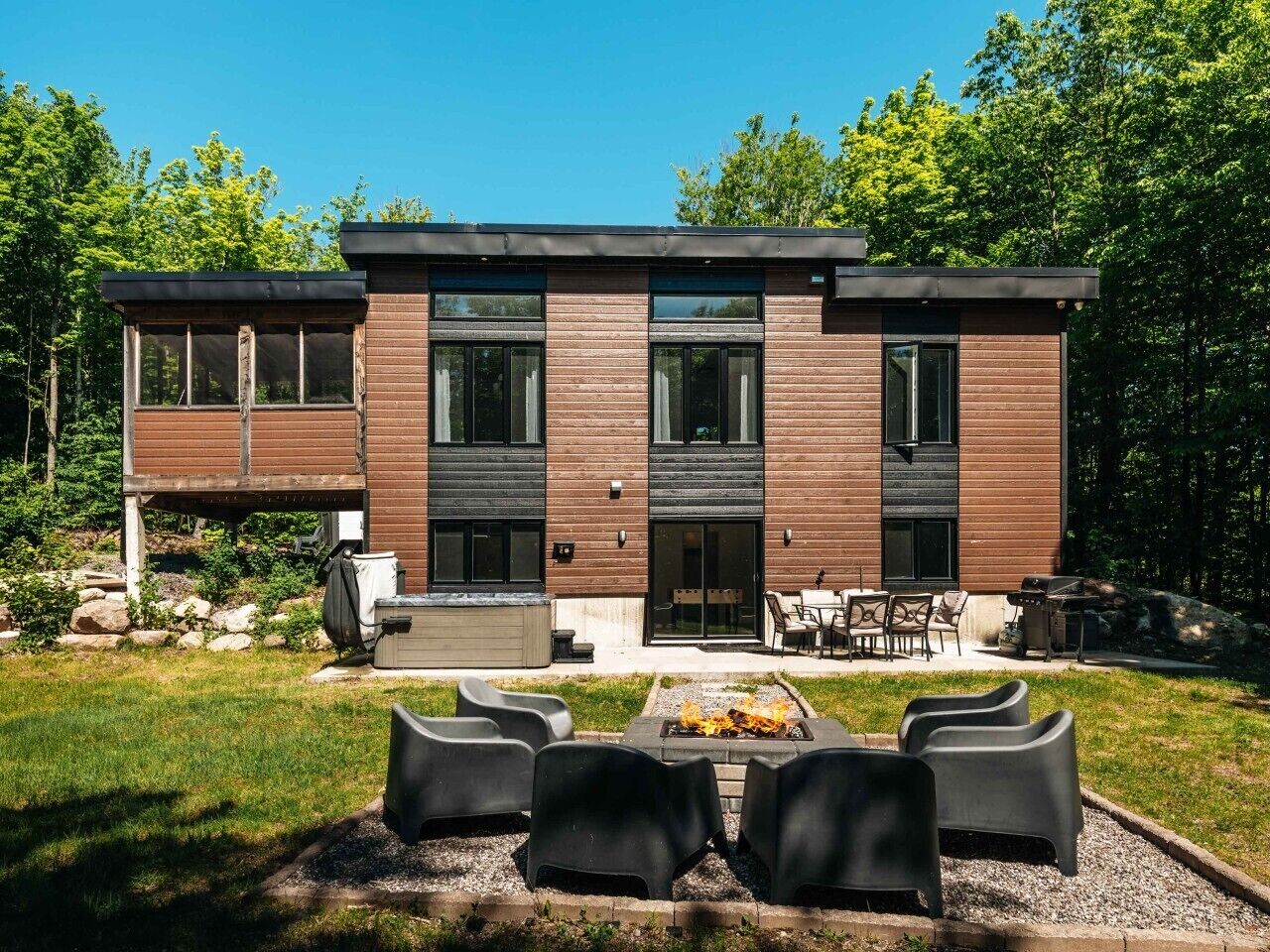 Una casa moderna de dos pisos con un patio, mobiliario exterior y un brasero.