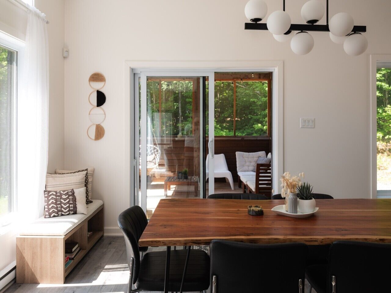 A dining area with a wooden table, black chairs, and a view of an outdoor deck through glass doors.