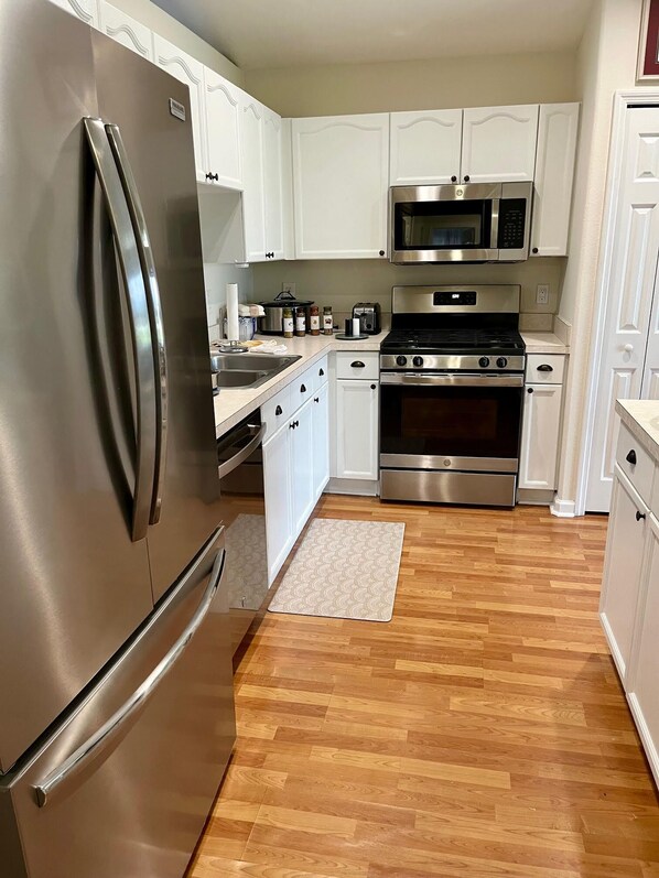 A modern kitchen with stainless steel appliances, white cabinetry, and a wooden floor. - Gated Community Close to Disney and attractions! No Pet Fee! (Clermont)