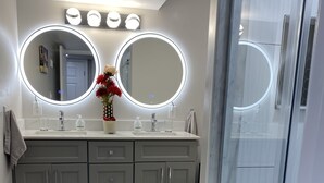 Une salle de bain moderne avec un meuble-lavabo, deux miroirs éclairés, un espace douche et un sol en marbre.