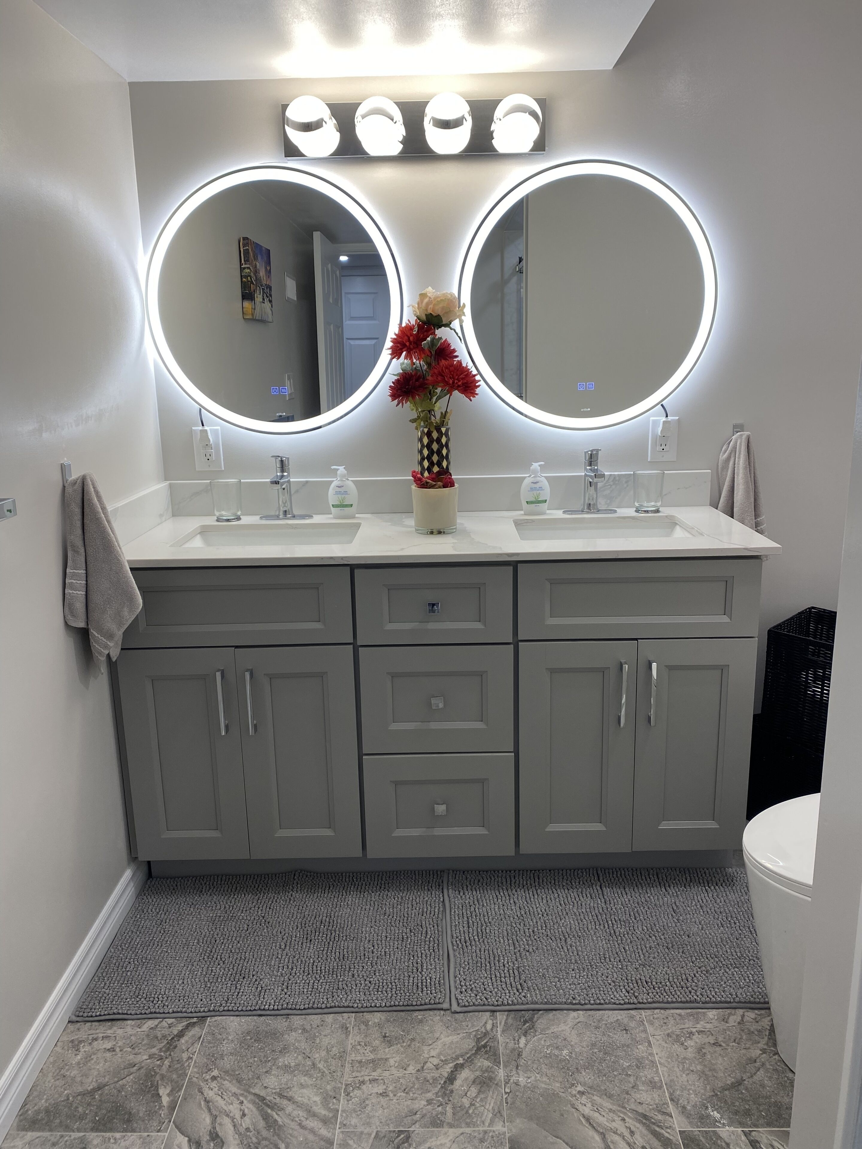 Een badkamer met twee wasbakken, een spiegel en een vaas met bloemen.