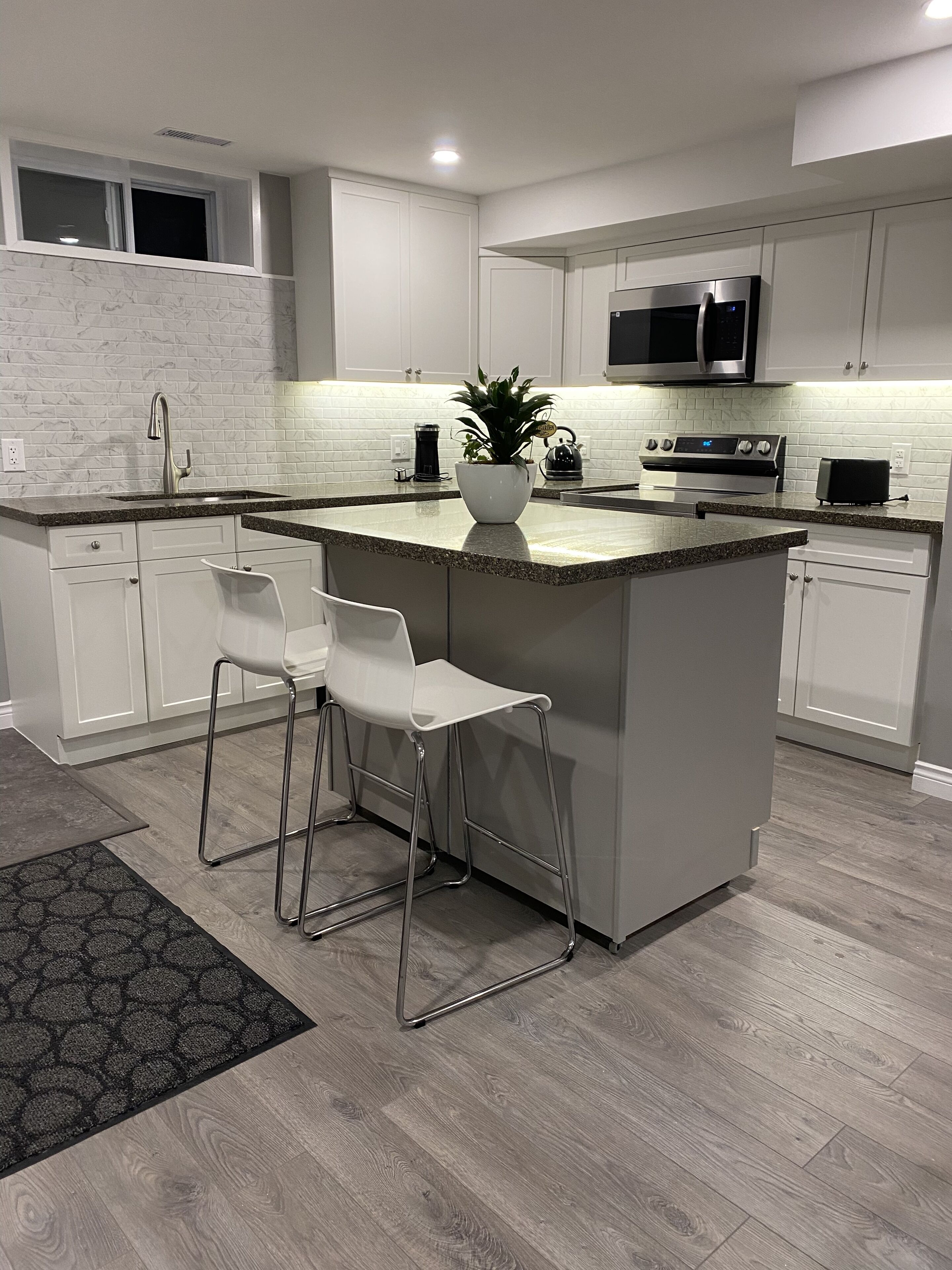 Une cuisine moderne avec des meubles blancs, un plan de travail en granit, des appareils en acier inoxydable et un îlot central doté de tabourets de bar.