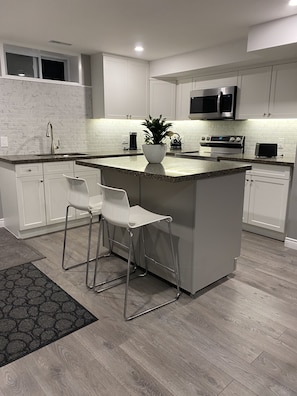 Una cocina moderna con armarios blancos, encimera de granito, electrodomésticos de acero inoxidable y una isla central con taburetes de bar.