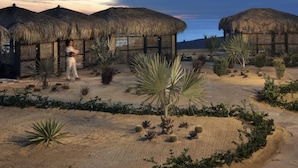 A desert landscape with thatched-roof huts, cacti, and a person walking.