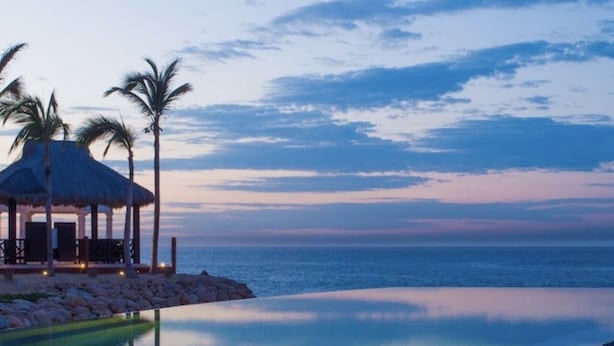 A beachside resort with a pool, palm trees, and a gazebo.