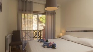 Quarto de hotel com uma cama grande, uma cadeira, um radiador e vista para o verde lá fora.