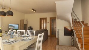 Uma sala de jantar com uma mesa posta para quatro pessoas, um sofá, uma escada e uma televisão na parede.