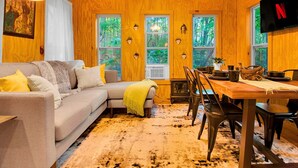 Un intérieur de chalet chaleureux avec un canapé, une table à manger, des chaises et un téléviseur.