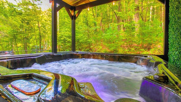 Un bain à remous situé dans une zone boisée, doté d’un toit en bois et offrant une vue sur la verdure environnante.