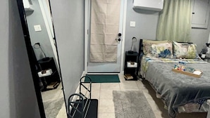Ein Schlafzimmer mit Bett, Nachttischen, einem Spiegel, einer Tür und einer Deckenleuchte.