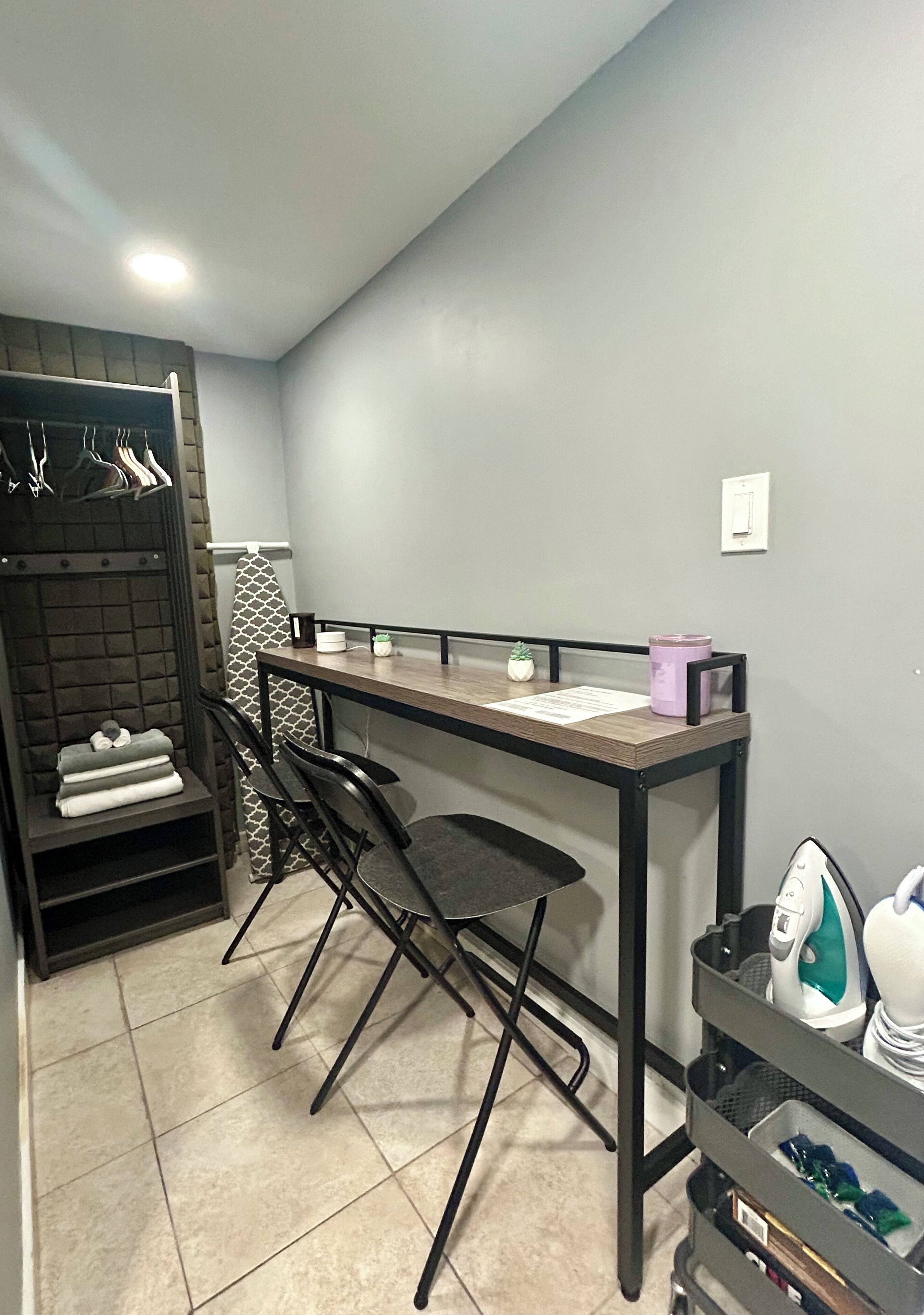 Habitación compacta con kitchenette, una pequeña mesa, dos sillas, armario empotrado y estante con toallas dobladas.