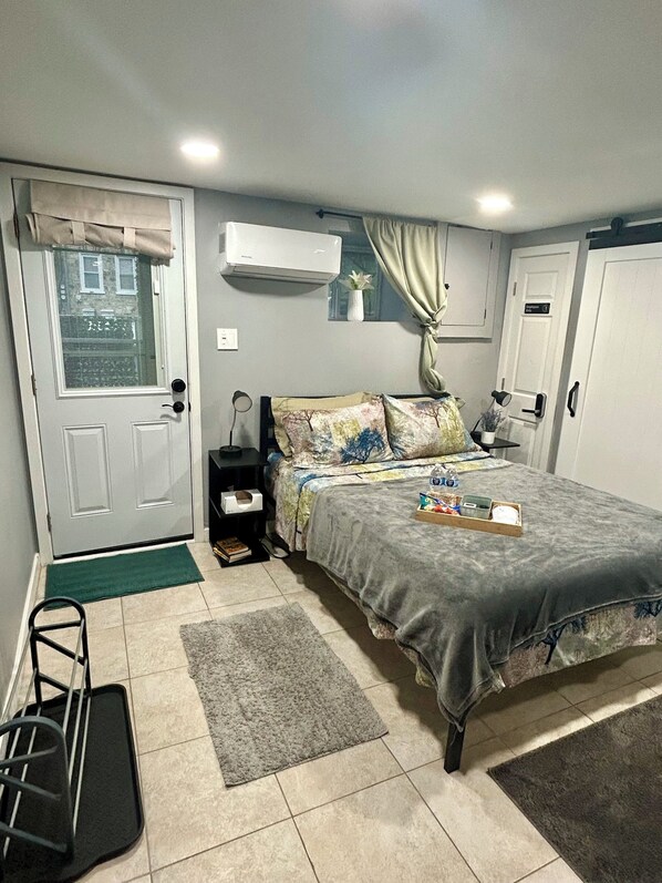 Une chambre à coucher comprenant un lit, des tables de chevet, une fenêtre avec des rideaux, un appareil de climatisation et une porte.
