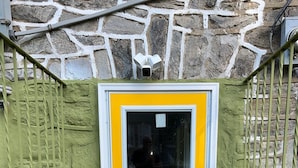 Eine gelbe Tür mit Fensterteil, eine Steinsäule und ein Metallgeländer.