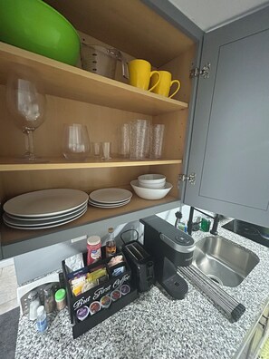 Een keuken met planken waarop borden, kommen, glazen en een koffiezetapparaat staan.