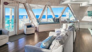 A spacious loft with a high ceiling and wooden beams, featuring a large window overlooking the ocean. - Oceanfront Seaside Stargazer+Hot Tub+Pets OK+Infinity Table+Beach Gear+4 Kings (North Topsail Beach)