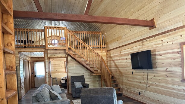 Een ruime loft-kamer met houten inrichting, een trap, een bank en een televisie.