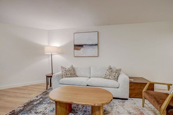 A modern living room with a sofa, a coffee table, a lamp, and a painting on the wall.