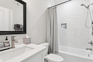 A modern bathroom with a white sink, toilet, and bathtub. There is a towel rack with towels, a mirror, and a shower curtain.