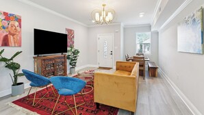 Una sala de estar moderna con televisor de pantalla plana, sofás azul y amarillo, alfombra roja estampada y un candelabro.