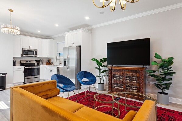 A modern kitchen with white cabinets, stainless steel appliances, and a flat-screen TV above a wooden cabinet.