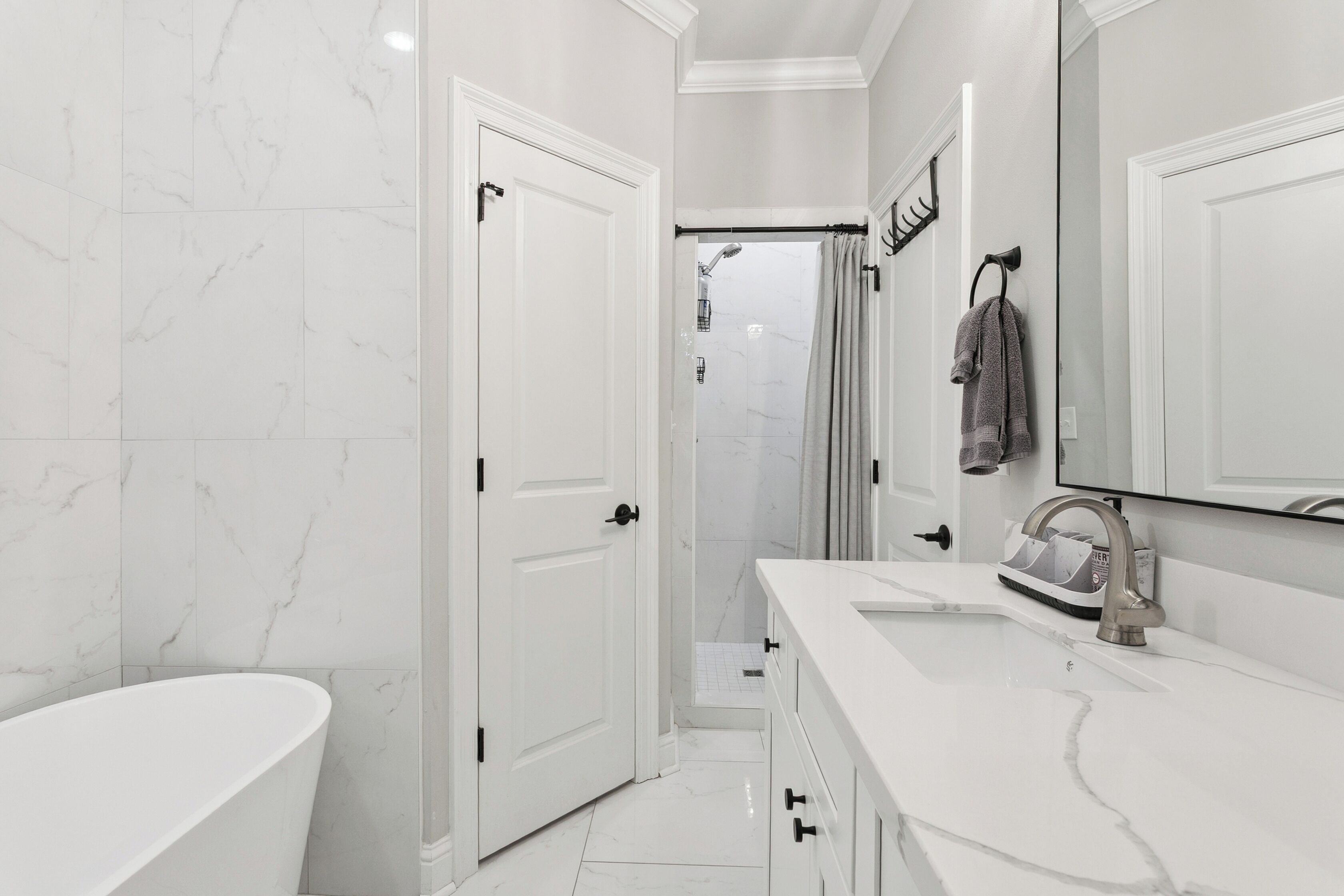 Een moderne badkamer met een vloer van wit marmer, een vrijstaand bad, een wastafel met een spiegel en een douchehoek.