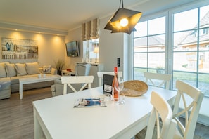 Una sala de estar moderna con un sofá blanco, una mesa de comedor con sillas, un ventanal con vistas al exterior y un cuadro en la pared.