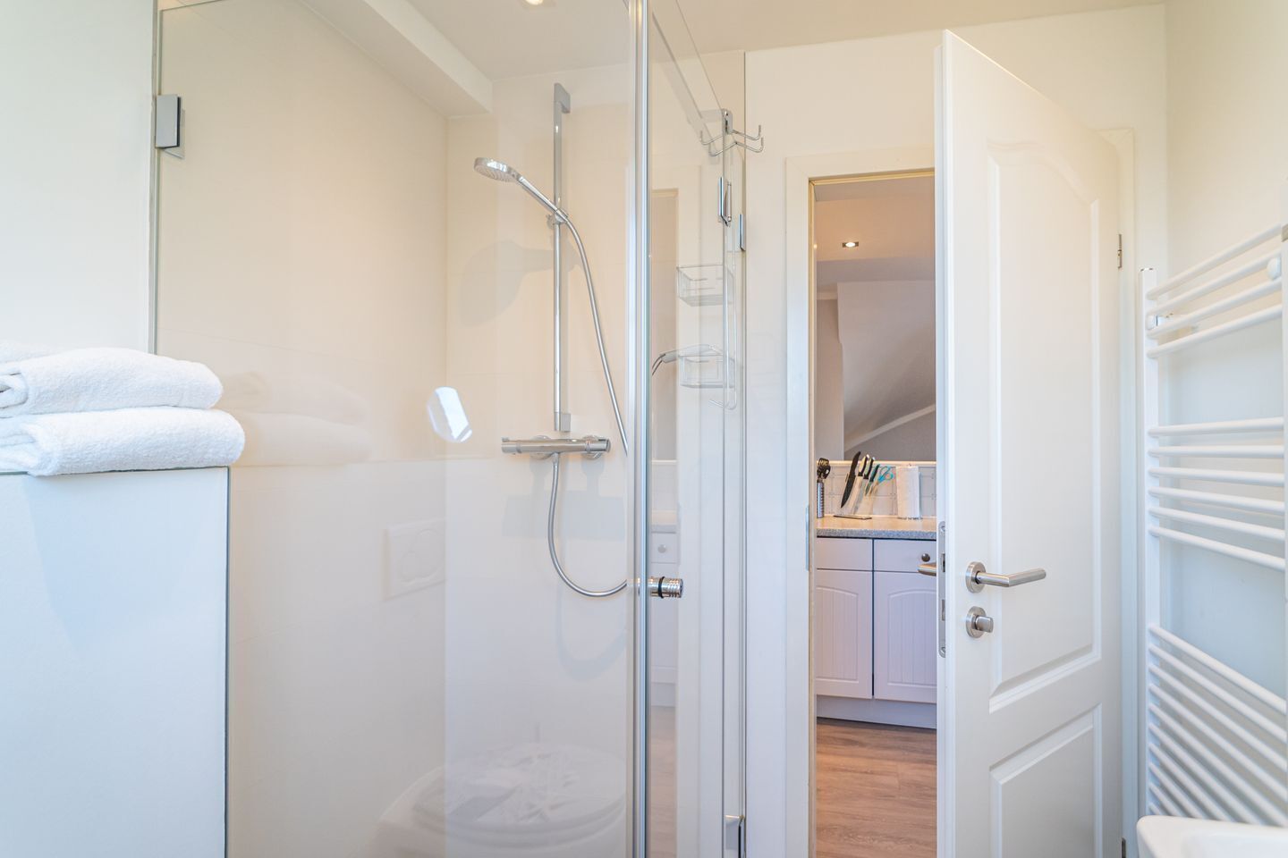 A modern bathroom with a glass shower enclosure, a white toilet, and a towel rack with folded towels.