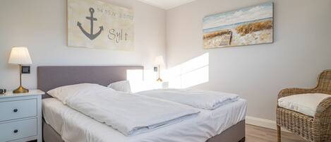 Un dormitorio con cama, mesitas de noche, lámpara, una silla y obras de arte en las paredes.