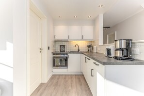 Una cocina moderna con gabinetes blancos, horno empotrado, cafetera y salpicadero de azulejos.