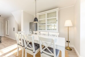 Un área de comedor con una mesa y sillas blancas, un aparador de vidrio arriba de la mesa y una lámpara de pie.