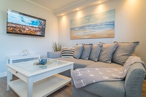 En moderne stue med en grå sofa, et glasbord og et maleri af en strandscene.