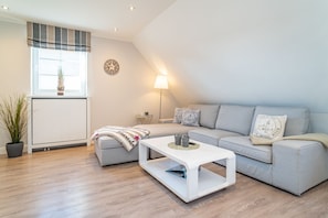 A modern living room with a grey sofa, a white coffee table, and a potted plant. - Appartement Dünenglück - Nicolinenhof - Appartement Dünenglück (Wenningstedt-Braderup (Sylt))