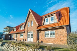 Une maison à deux étages, construite en briques, avec un toit recouvert de tuiles rouges, une entrée centrale dotée de deux portes et un petit jardin à l’avant.