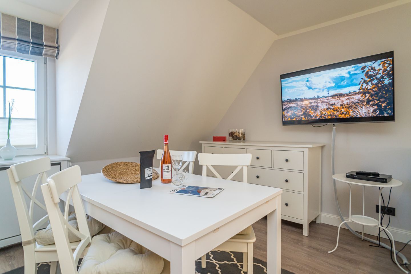 A modern, well-lit room with a dining table, chairs, a TV, and a small side table.