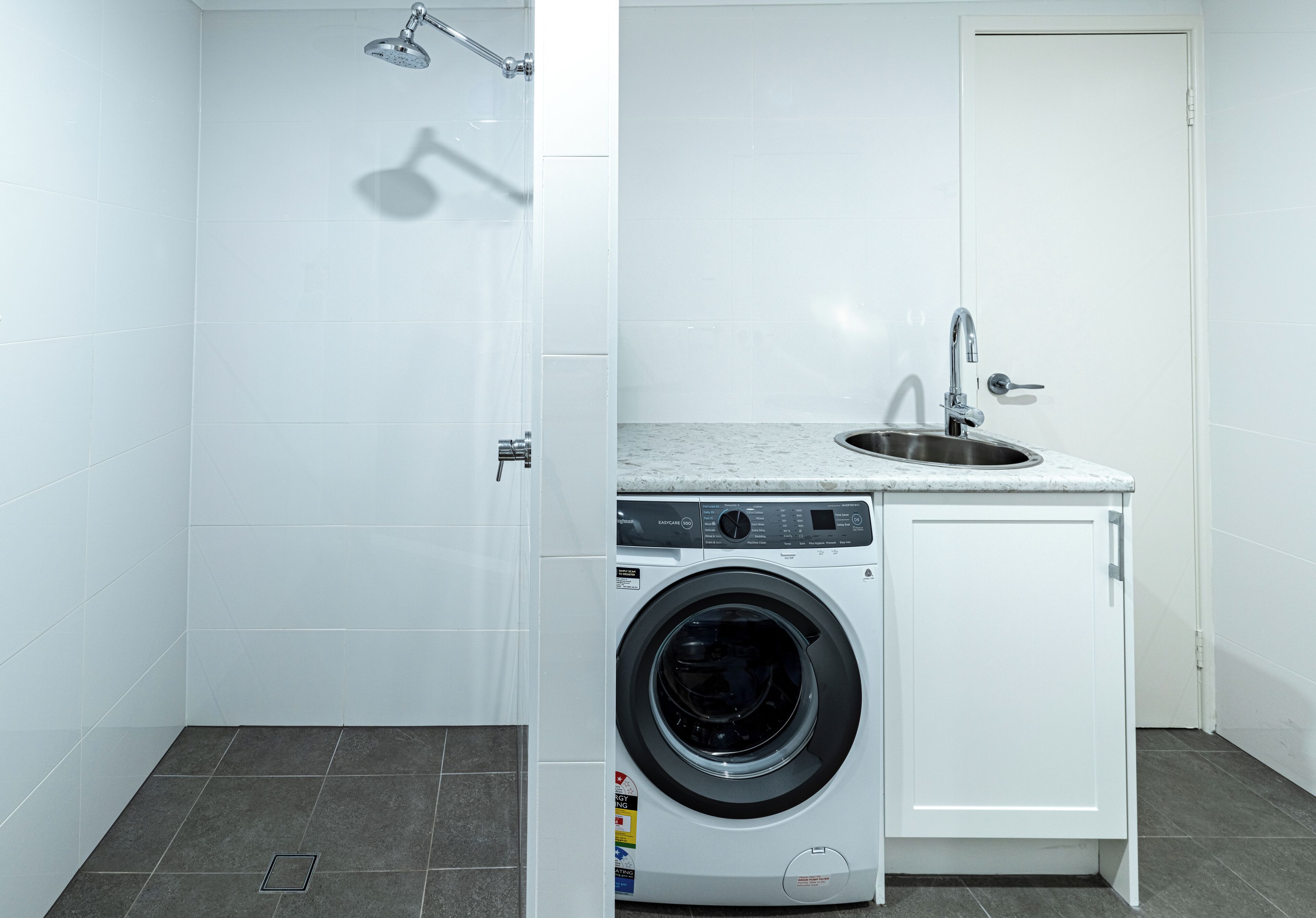A compact laundry room with a washing machine, a sink, and a shower.