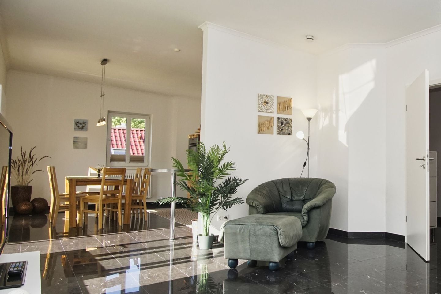 A modern living room with a dining area, a green armchair, and a potted plant.