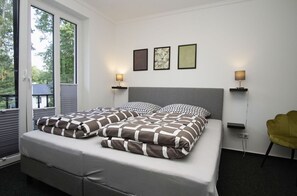 Ein Schlafzimmer mit einem großen Bett, zwei Nachttischen mit Lampen, einem Sessel und einem Fenster mit Jalousien.