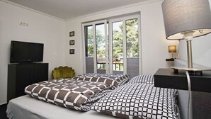 Een slaapkamer met een bed, een televisie, een lamp en een raam met uitzicht op bomen.