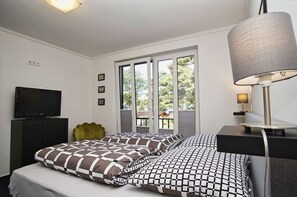 A bedroom with a bed, a TV, a lamp, and a window with a view of trees. - Ferienwohnung Cosmo - Direkt am Waldrand mit Balkon und in Strandnähe - Ferienwohnung Cosmo (Glowe)
