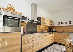 A modern kitchen with stainless steel appliances, wooden cabinets, and a built-in oven. - Ferienwohnung Cosmo - Direkt am Waldrand mit Balkon und in Strandnähe - Ferienwohnung Cosmo (Glowe)