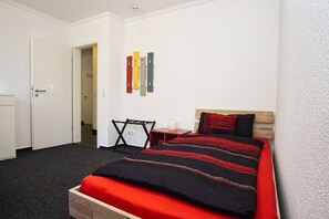 A bedroom with a bed, a desk, and a chair. There are storage cabinets and a door. - Ferienwohnung Cosmo - Direkt am Waldrand mit Balkon und in Strandnähe - Ferienwohnung Cosmo (Glowe)