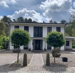 Ein modernes, zweistöckiges Haus mit einer symmetrischen Fassade, großen Fenstern und einem zentralen Eingang.