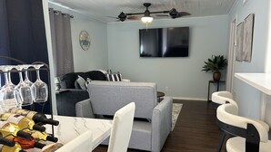 A modern living room with a grey sofa, a dining table with white chairs, a TV mounted on the wall, and a ceiling fan. - The Dolce Cabana located on the golf course in beautiful Diamondhead, MS. (Diamondhead)